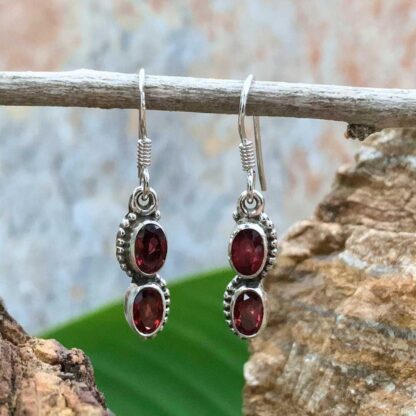 an image of a pair of dangle earrings with two oval faceted garnet gemstones and set in sterling silver