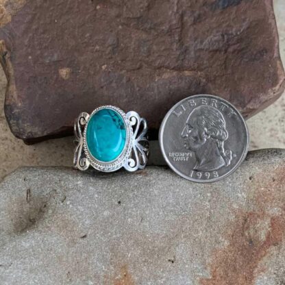 an image of an oval Turquoise ring in sterling silver with elegant filigree work on the sides. The ring is next to a quarter