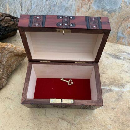 an image of a Pirate Trunk style Keepsake Box handcrafted of wood in a dark burgundy color with black trim. Made in Poland. Dimensions are 5.50 x 3.50 x 3.50 inches. This is an inside view showing the red velvet lining and a key to lock the trunk.