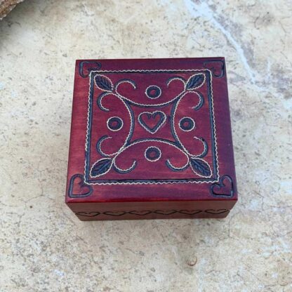 an image of a Small Handcrafted Burgundy Wood Hearts Keepsake Box with a heart in each corner and one in the center and hearts carved all around the side. Dimensions are 3 x3 inches square x 1.5 inches high.