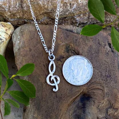 an image of a Petite Sterling Silver Treble Clef Pendant next to a dime