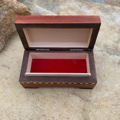 an image of the inside of small handcrafted brown trunk keepsake box with a floral design on the top and a circular pattern on the ends and around the sides. The dimensions are Length: 4.188 inches x Width: 2.125 inches x Height: 2 inches. The inside has a red velvet lined bottom