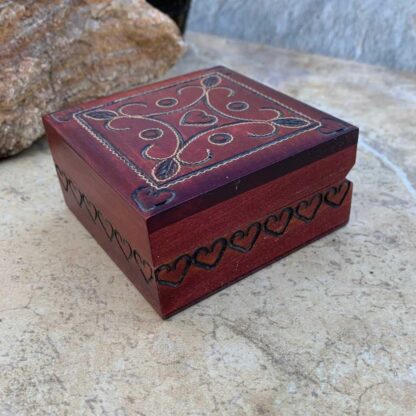 an image of a Small Handcrafted Burgundy Wood Hearts Keepsake Box with a heart in each corner and one in the center and hearts carved all around the side. Dimensions are 3 x3 inches square x 1.5 inches high.