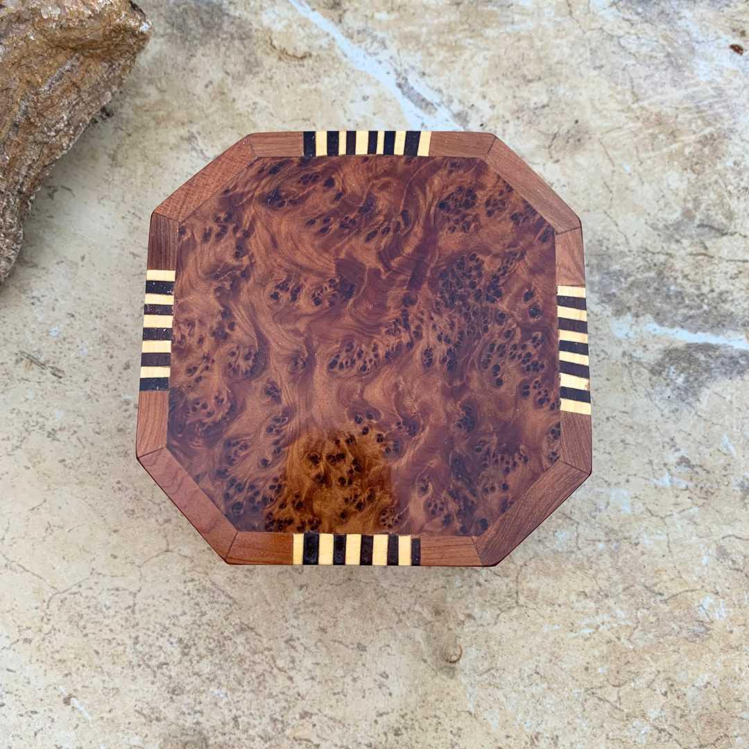 an image of an Octagon Shaped Moroccan Thuya and Lemon Wood Box. The top has beautiful burl wood and four sides have a striped inlay pattern of yellow lemon wood with lemon wood that has been dyed black. The dimensions are 4.5 x 4.5 x 2 inches.