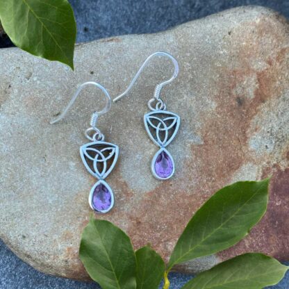 an image of a pari of sterling silver dangle earrings with a Celtic Trinity or Triquetra knot at the top and a teardrop shaped faceted amethyst dangling from the bottom.