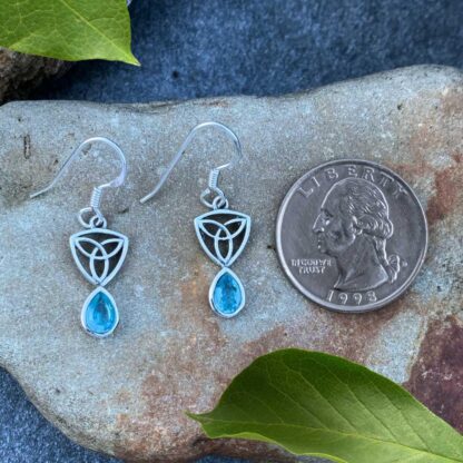 an image of a pari of sterling silver dangle earrings with a Celtic Trinity or Triquetra knot at the top and a teardrop shaped faceted blue topaz dangling from the bottom.