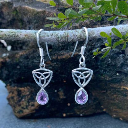 an image of a pari of sterling silver dangle earrings with a Celtic Trinity or Triquetra knot at the top and a teardrop shaped faceted amethyst dangling from the bottom.