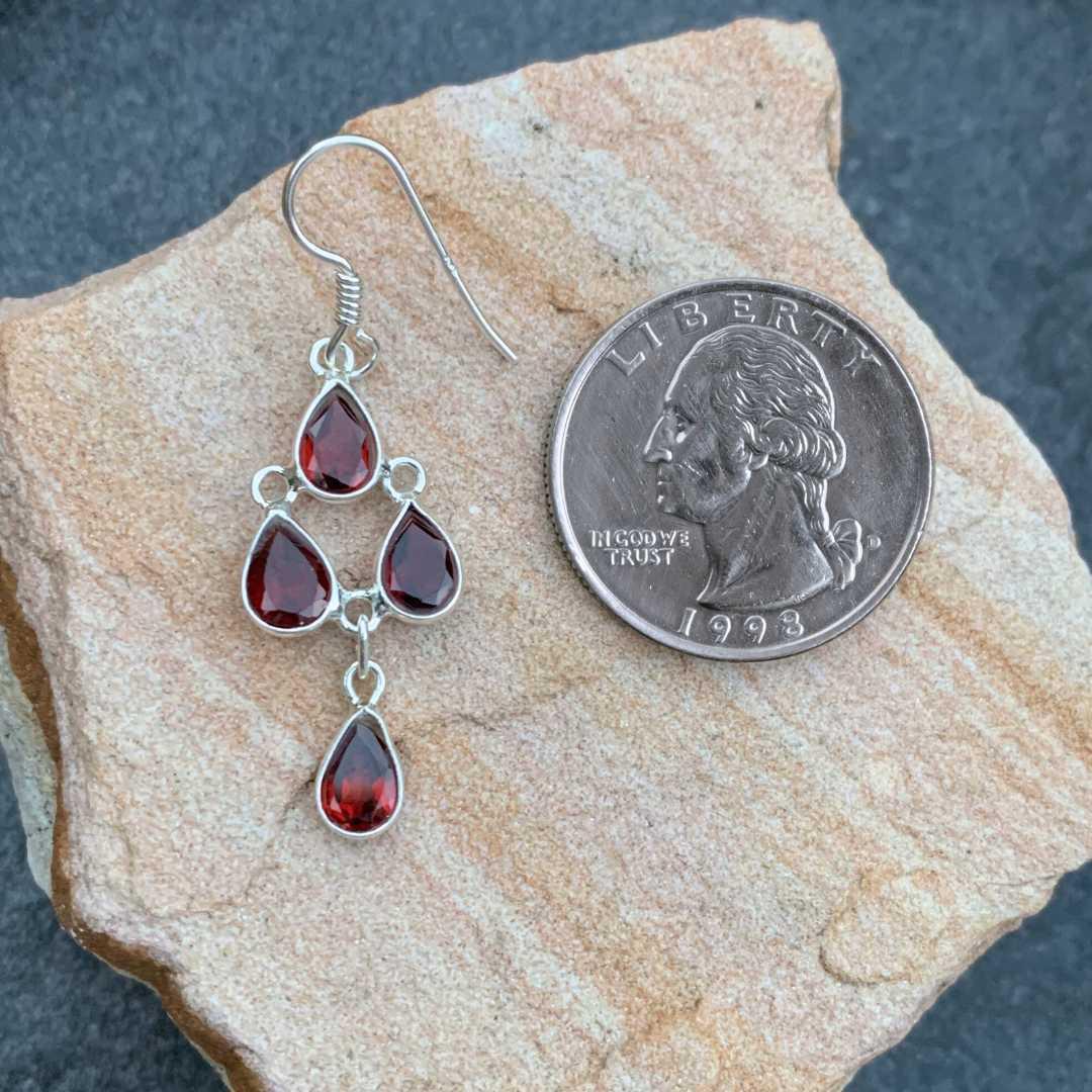 an image of a Garnet and Sterling Silver Chandelier Earring with four teardrop faceted garnet gemstones dangling down and laying next to a quarter
