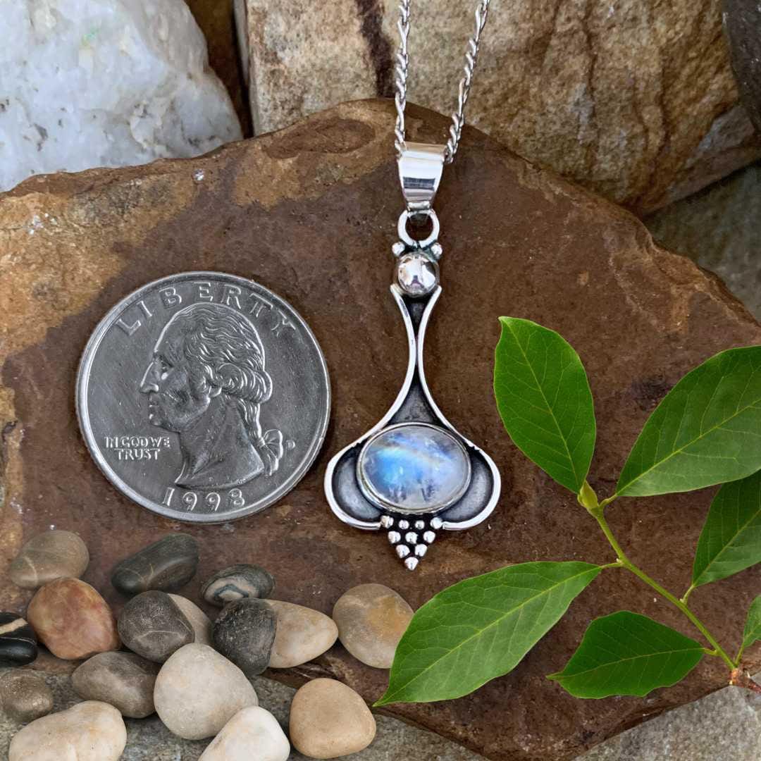 an image of a Oval Rainbow Moonstone and Sterling Silver Beaded Pendant next to a quarter