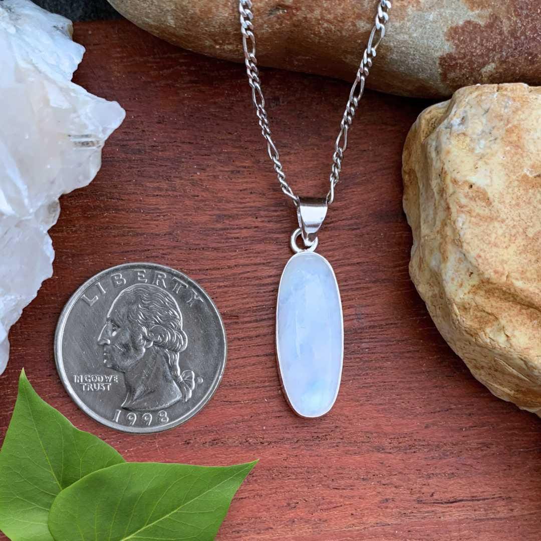 an image of an Oblong Rainbow Moonstone and Sterling Silver Pendant next to a quarter