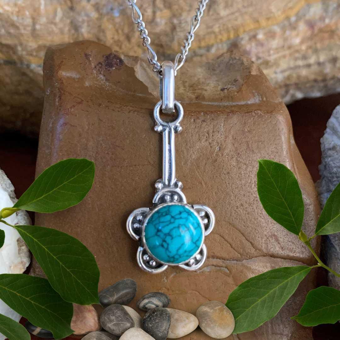 An image of a round turquoise stone surrounded a sterling silver flower shape handing from a sterling silver stem