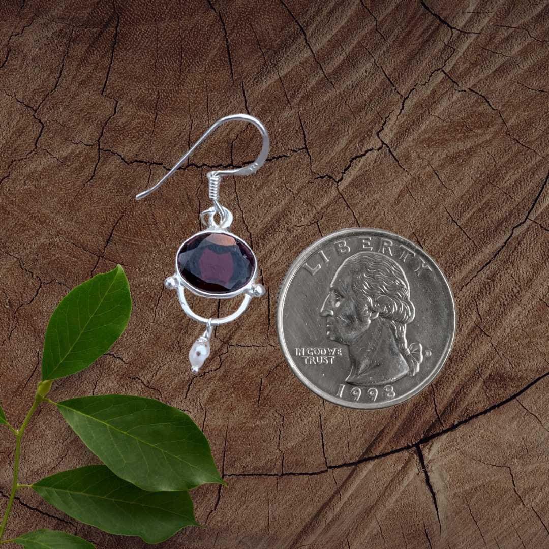 an image of a pair of Oval Garnet with a tiny Pearl and Sterling Silver Earrings next to a quarter
