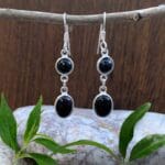 an image of a pair of dangle earrings with a smaller round black onyx cabochon and below it a larger oval black onyx cabochon all set in sterling silver