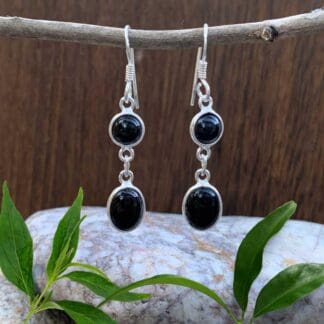 an image of a pair of dangle earrings with a smaller round black onyx cabochon and below it a larger oval black onyx cabochon all set in sterling silver