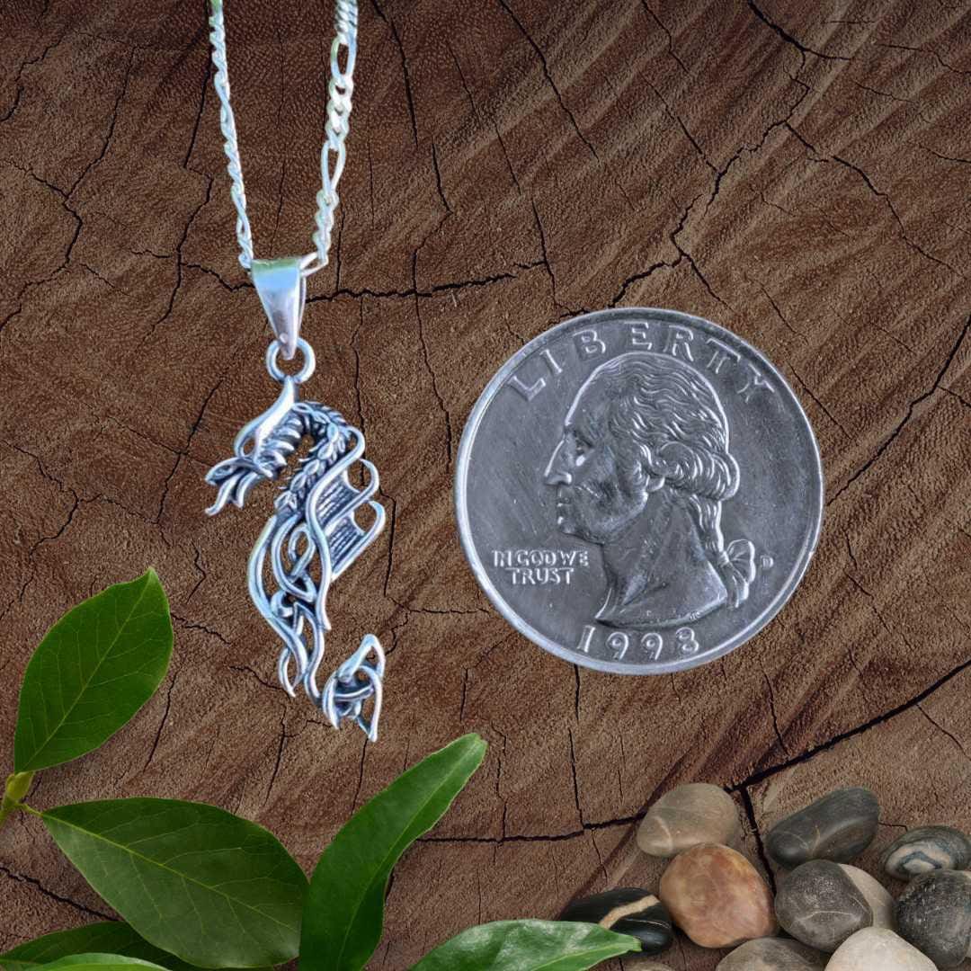 an image of a vertical designed sterling silver dragon pendant with fire out of the mouth and some celtic knots in the design next to a quarter