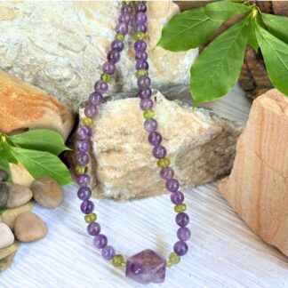 an image of a Amethyst and Peridot Beaded Necklace with a larger focal piece at the center and round amethyst beads alternating with peridot beads. It is finished with sterling silver beads and lobster clasp