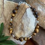 an image of a 7.25 inch long Tiger's Eye bracelet made with 3 sizes of round beads and four dainty silver beads with a primitive flower hand stamped and made by Karen Hill Tribe in Thailand. There is a sterling silver lobster clasp.