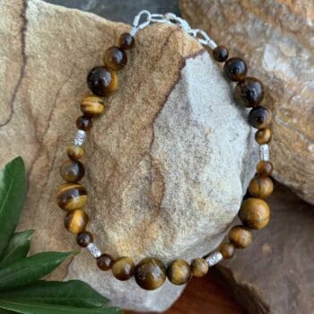 an image of a 7.25 inch long Tiger's Eye bracelet made with 3 sizes of round beads and four dainty silver beads with a primitive flower hand stamped and made by Karen Hill Tribe in Thailand. There is a sterling silver lobster clasp.