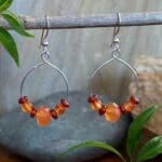 an image of a pair of Carnelian and Sterling Silver Dangle Hoop Earrings. There is an open circle with some carnelian beads on it and the hoop hangs from an ear hook