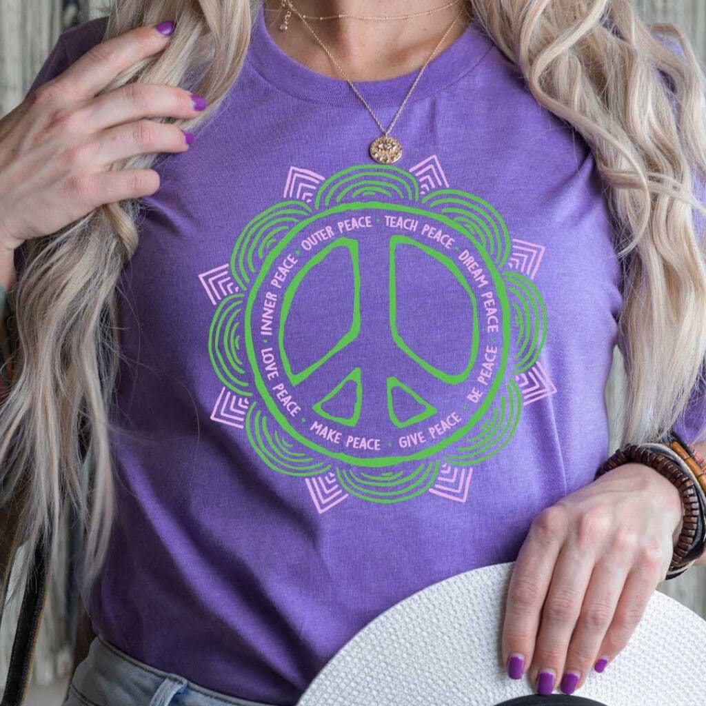 An image of a purple T shirt with a green and pink mandala style peace sign