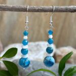 an image of a pair of Apatite and Mother of Pearl Beaded Earrings featuring a 10 mm smooth round apatite bead at the bottom with mother of pearl heishi beads alternating with smaller apatite beads. They are on sterling silver earring hooks and have a medium dangle