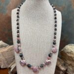 an image of a Rhodochrosite Teardrops and Larvikite Necklace featuring 5 teardrop shaped rhodochrosite beads accented with a mix of faceted grey larvikite beads and rhodochrosite beads offering a lovely combination of the pinks and greys. The necklace is 18.875 inches long.