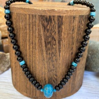 an image of an Apatite and Black Onyx Necklace featuring one large faceted rondelle of blue apatite in the center and rondelle and round black onyx beads working up the neck with occasional apatite heishi beads interspersed.