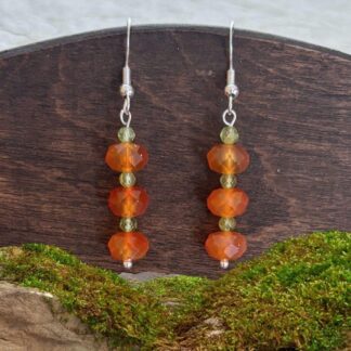 an image of a pair of Faceted Carnelian and Peridot Dangle Earrings that have three faceted carnelian rondelle shaped beads stacked with small faceted peridot beads in between. They hand on a sterling silver ear hook with a medium amount of dangle.