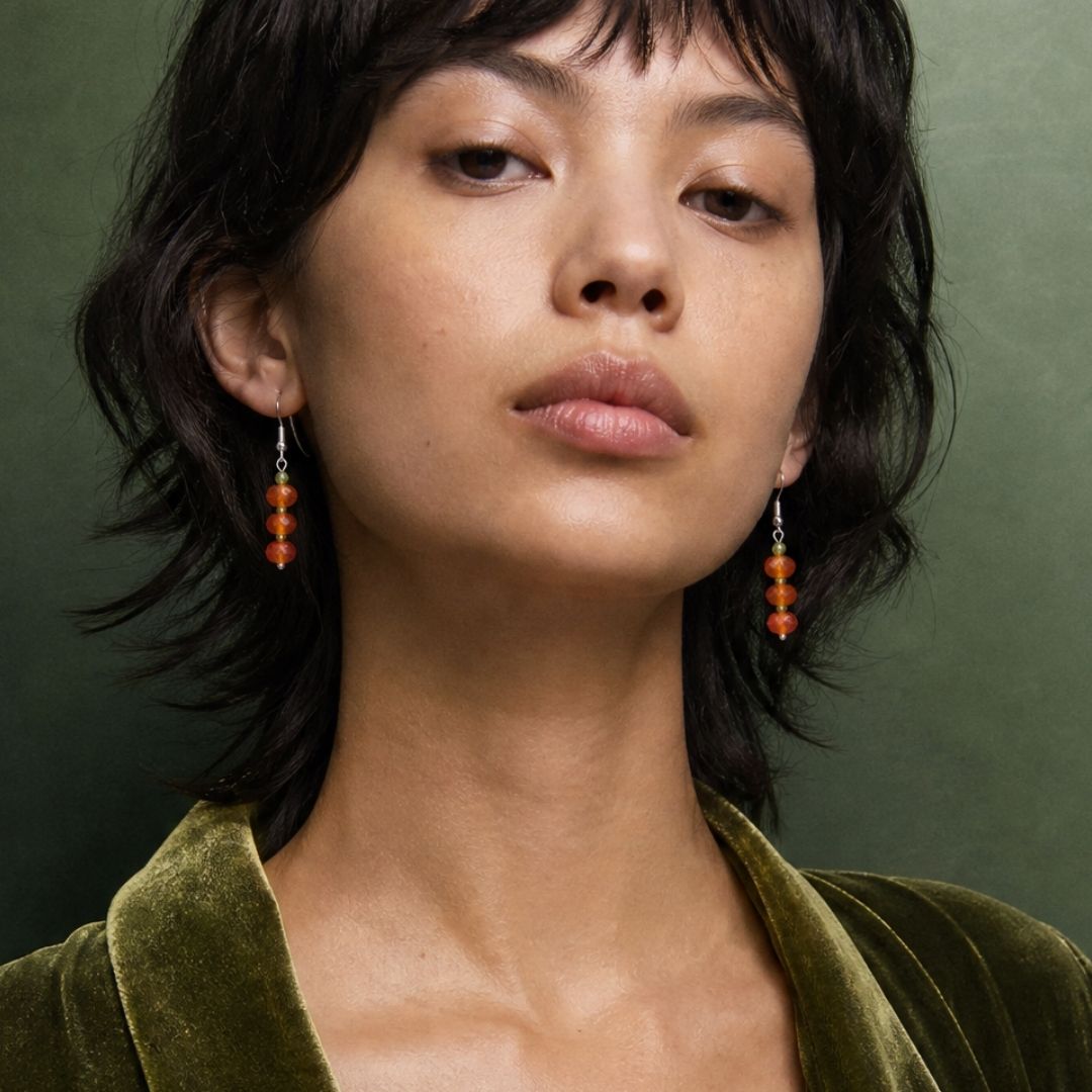an image of an AI model wearing our Faceted Carnelian and Peridot Dangle Earrings. The earrings have three faceted rondelle orange carnelian beads separated by 4 mm faceted peridot beads.