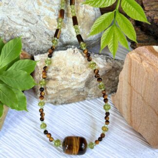 an image of a Tiger's Eye and Peridot Beaded Necklace featuring a large tiger's eye barrel bead as the focal center with alternating smaller peridot and tiger's eye beads working up the neck. It is finished off with sterling silver beads and lobster clasp.