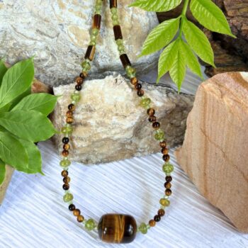 an image of a Tiger's Eye and Peridot Beaded Necklace featuring a large tiger's eye barrel bead as the focal center with alternating smaller peridot and tiger's eye beads working up the neck. It is finished off with sterling silver beads and lobster clasp.