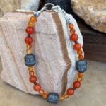 an image of a Gemstone beaded bracelet with 3 hematatite grey buddha head beads and orange and golden carnelian beads